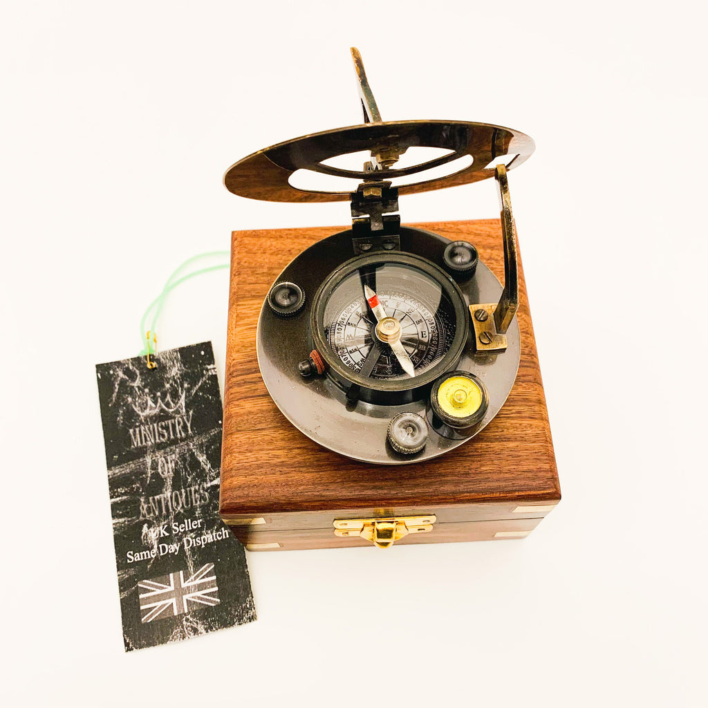 Peut inclure: Un compas et un cadran solaire en laiton dans une boîte en bois. Le compas a un cadran noir avec des marques blanches et une aiguille rouge. Le cadran solaire a un cadran en laiton avec un pointeur noir. La boîte est en bois foncé avec un loquet en laiton.