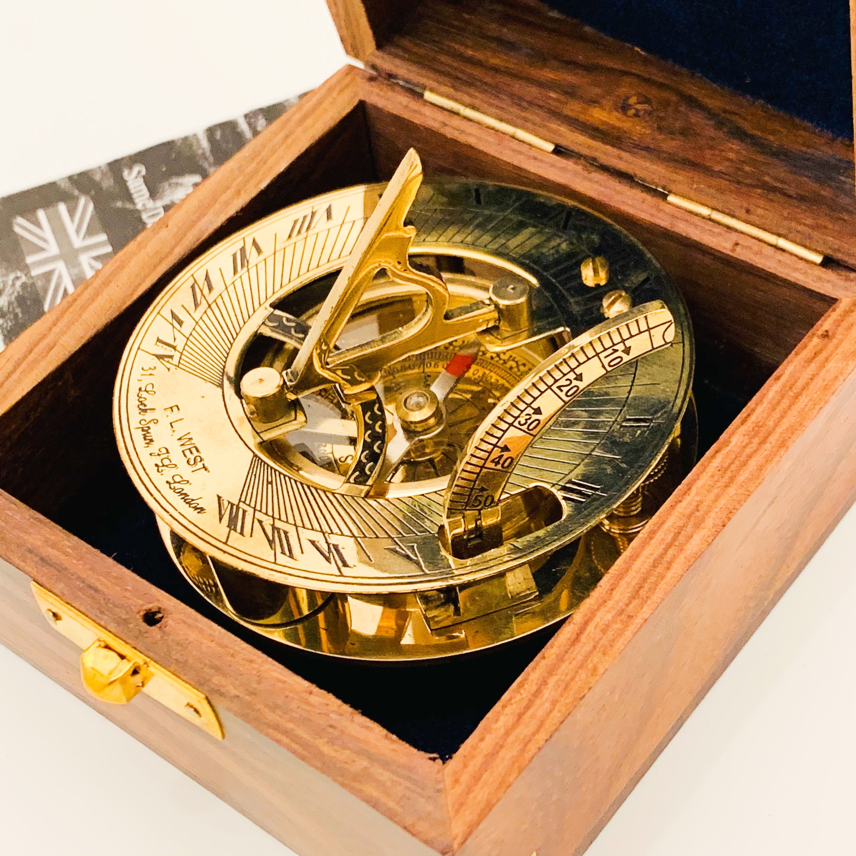 May include: A brass sundial with a compass and a wooden box. The sundial has Roman numerals and a scale marked in degrees. The box is made of dark wood with a brass latch.