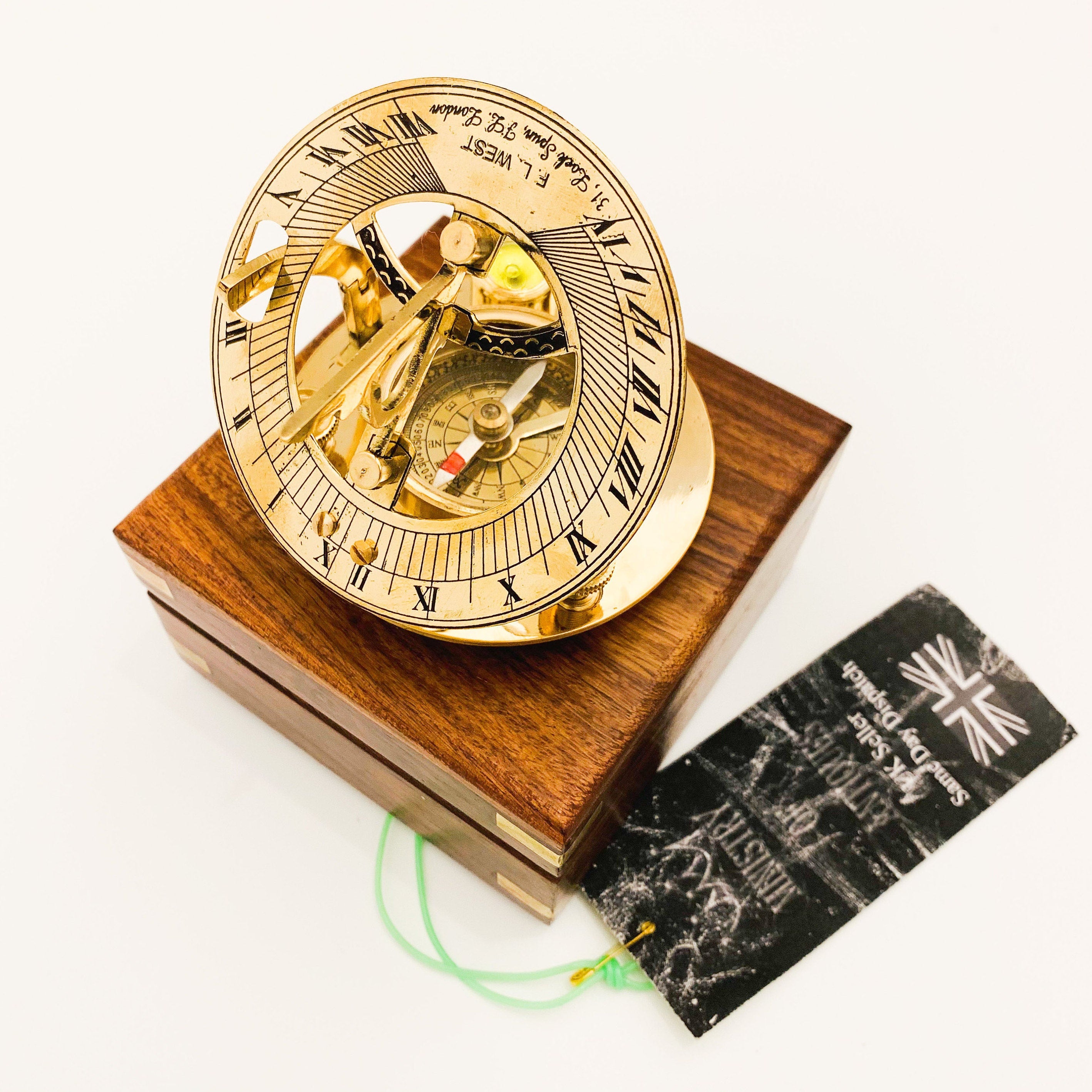 May include: A brass sundial with a compass in the center, set on a wooden box. The sundial has Roman numerals and is inscribed with "F.L. WEST VIVE XVIII 31, Lock Spun, FL, London".
