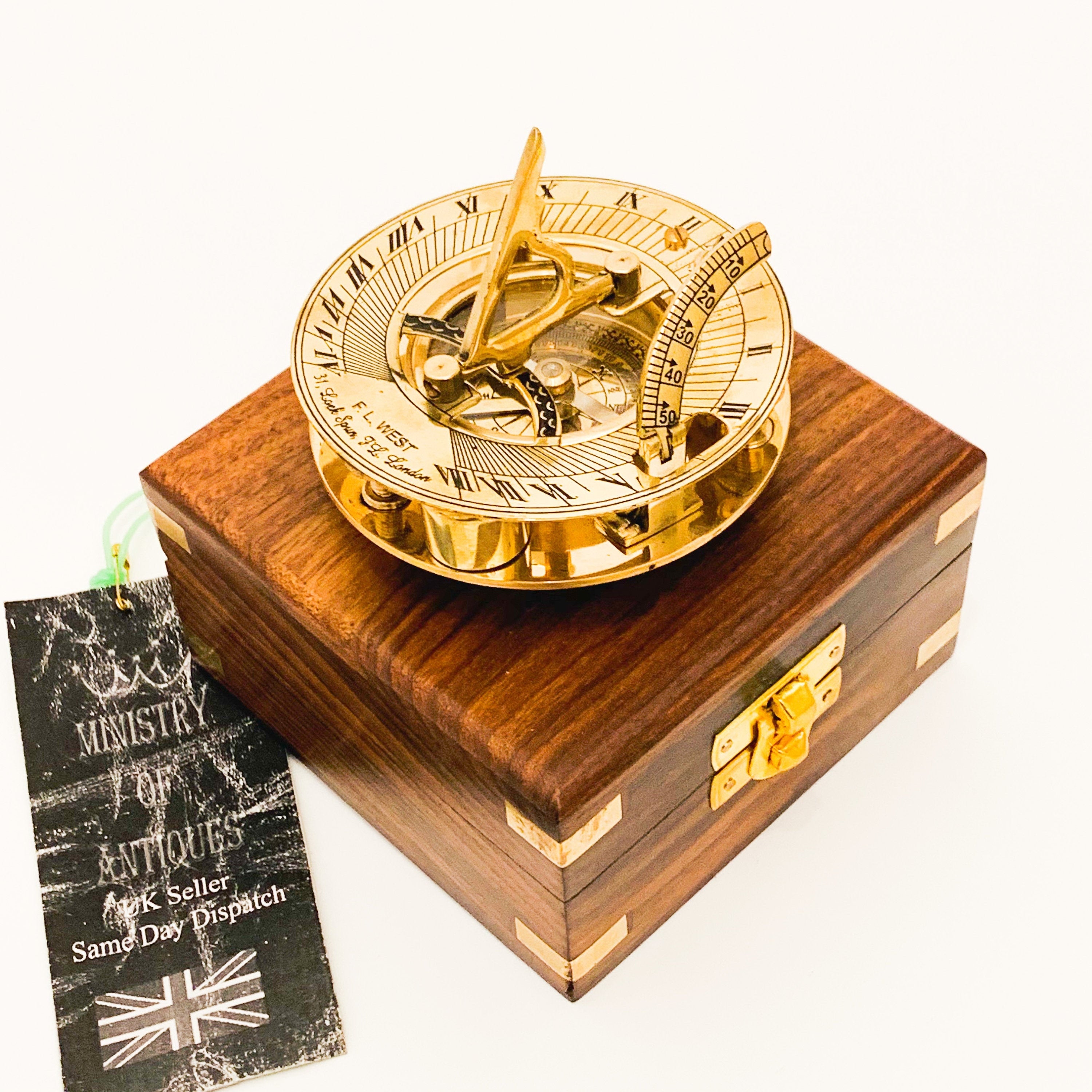 May include: A brass sundial with a compass and a wooden box. The sundial has Roman numerals and a compass rose. The box is made of dark wood with brass accents.