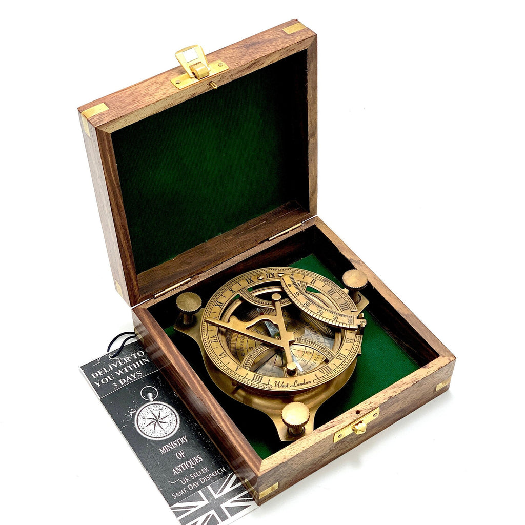 May include: A brass sundial compass in a wooden box with a green felt lining. The compass has a compass rose, hour markings, and a sundial. The box has a brass latch and hinges.