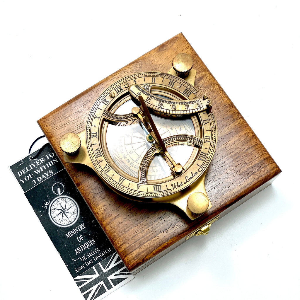 May include: A brass sundial with a compass and a wooden box. The sundial features Roman numerals and a compass rose. The box is made of dark wood and has a brass latch.