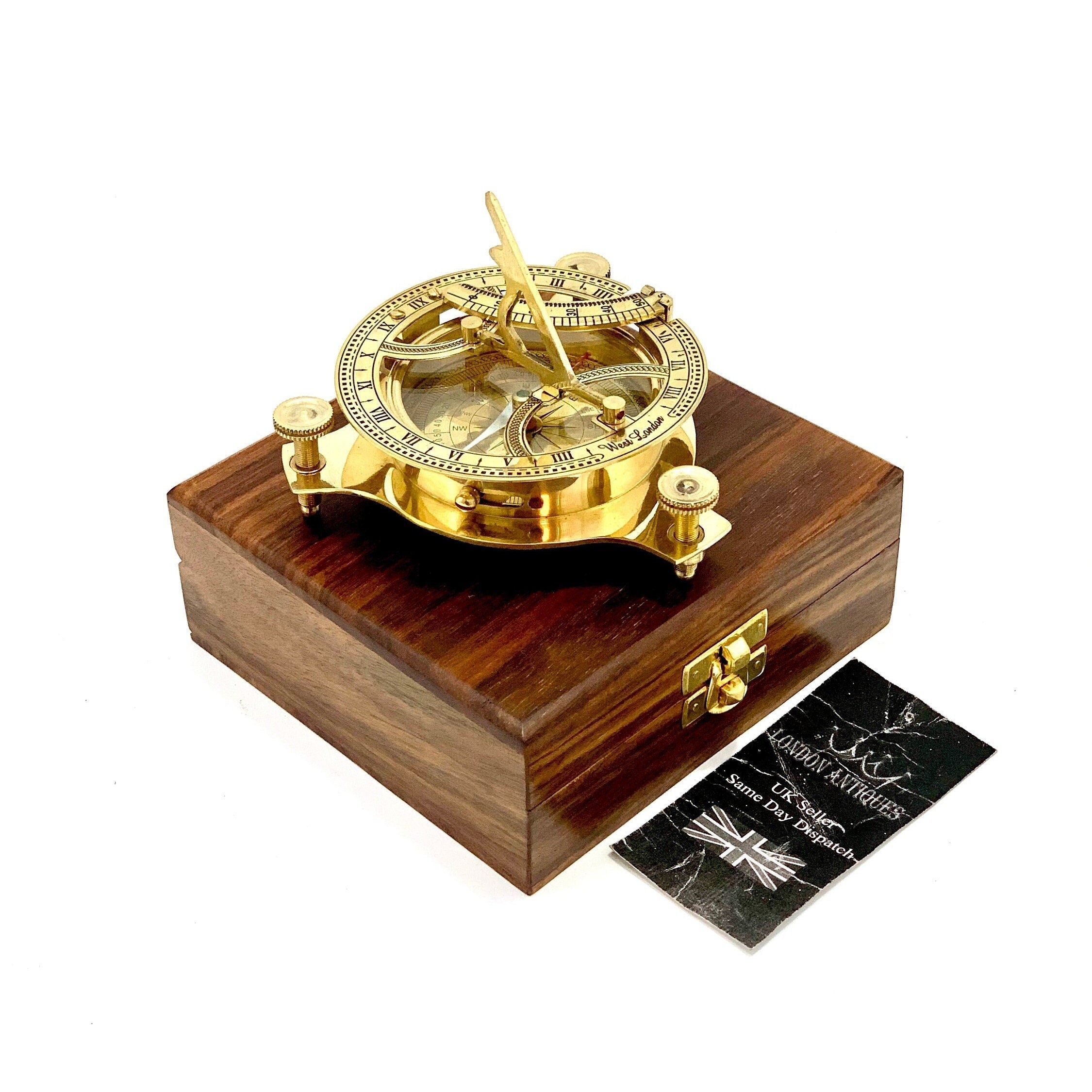 May include: A brass sundial compass with a wooden box. The compass has a clear glass face with Roman numerals and a compass rose. The box is made of dark wood with a hinged lid.