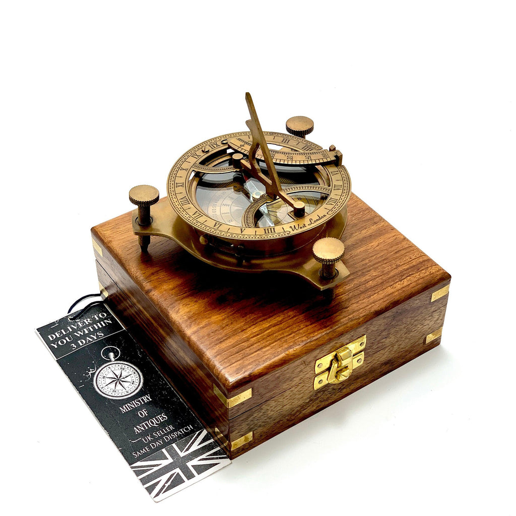 May include: A brass compass and sundial with a wooden box. The compass has a clear face with Roman numerals and a compass rose. The sundial has a brass needle and a clear face with Roman numerals. The box is made of dark wood with brass accents.