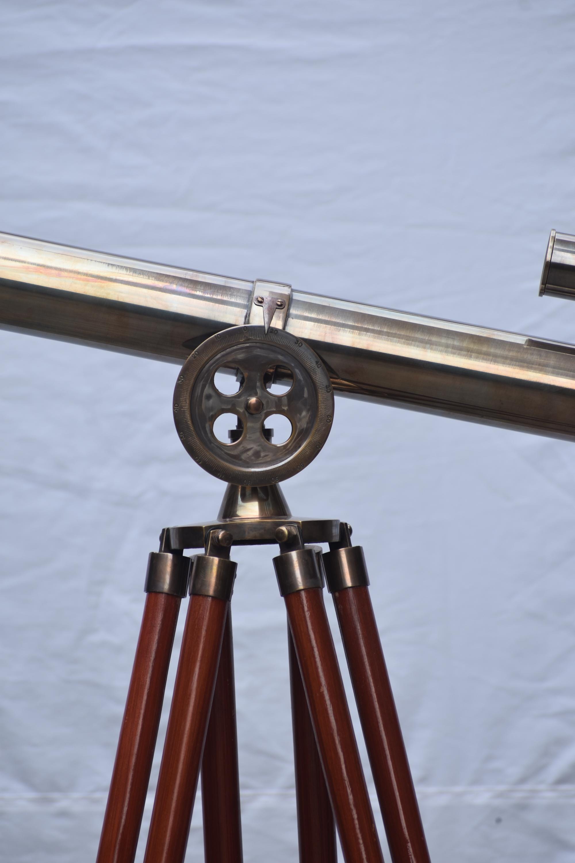 May include: A brass telescope on a wooden tripod. The telescope features a long, cylindrical barrel and a circular adjustment wheel. The tripod legs are dark brown and angled outwards for stability.