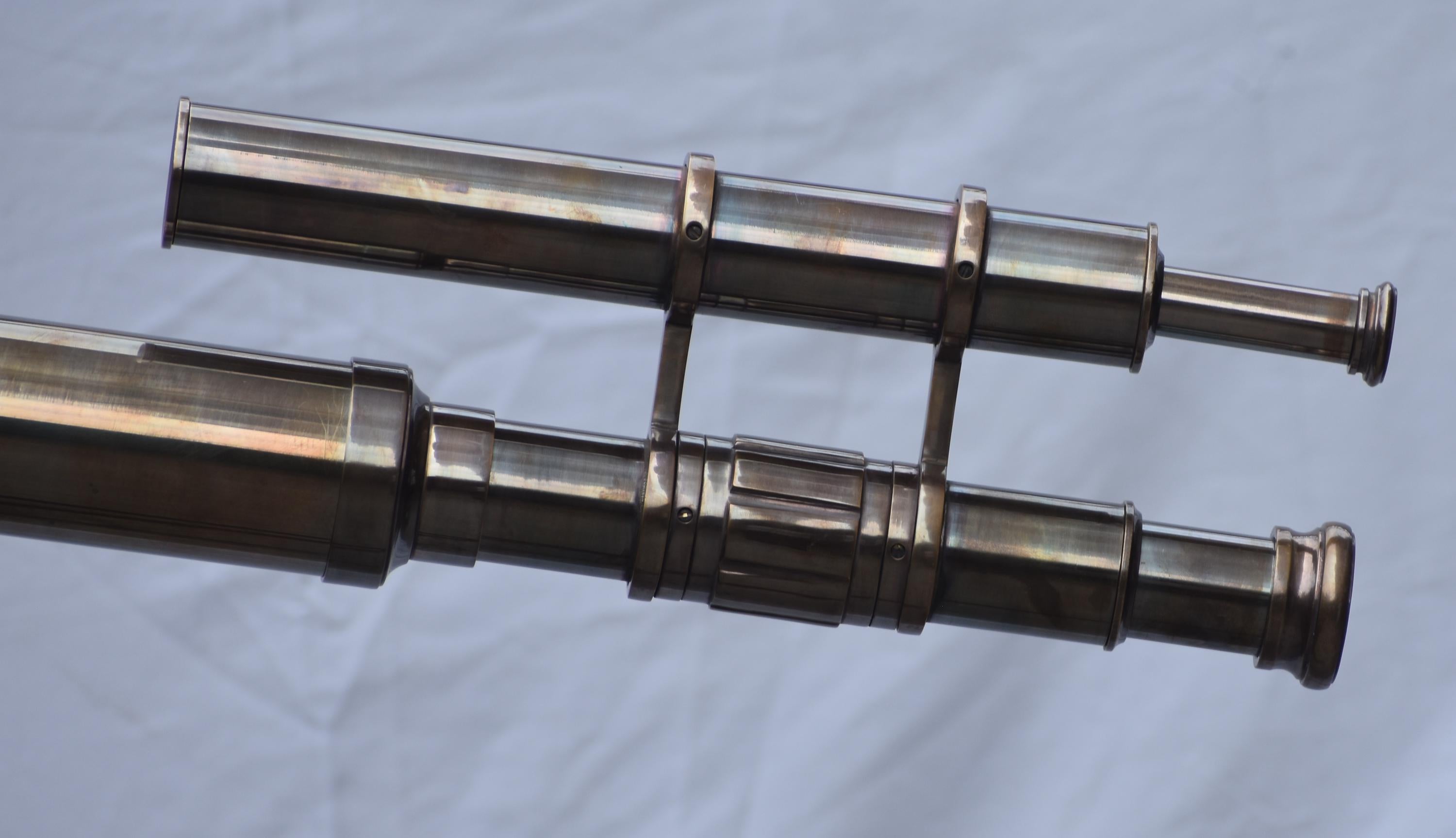 May include: A vintage brass telescope with two parallel tubes. The telescope has a classic design with multiple sections and rings. The brass has a warm, aged patina, suggesting it is an antique or a replica of an antique.