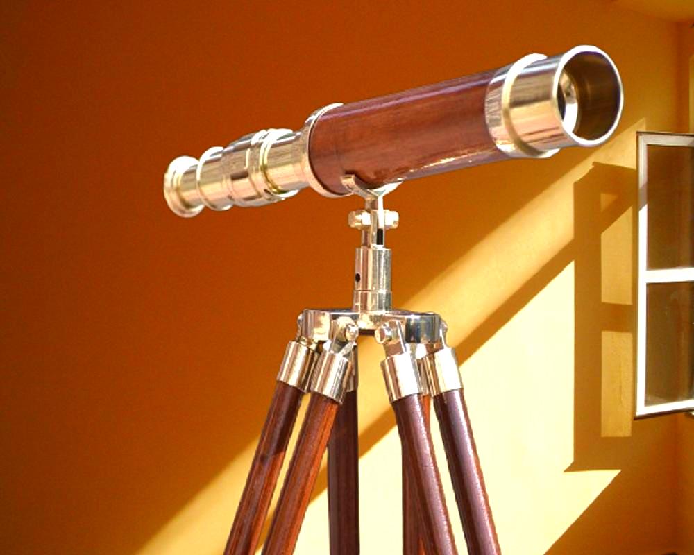 May include: A vintage telescope with a wooden barrel and brass detailing. It is mounted on a tripod with wooden legs and brass fittings. The background is a warm, orange-toned wall.