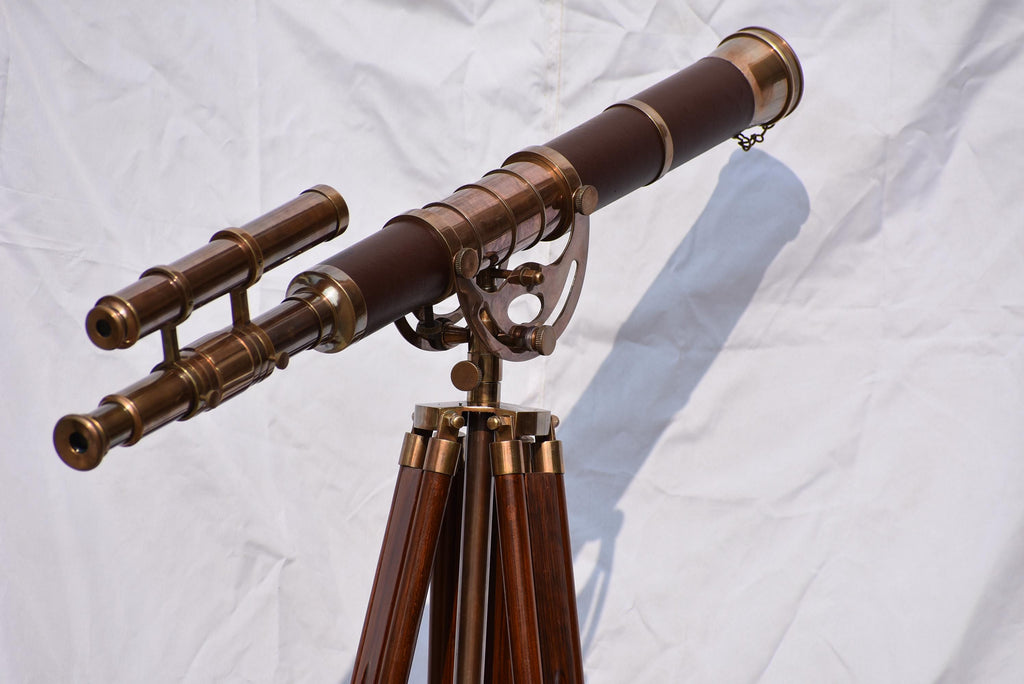 May include: A vintage-style telescope with a dark brown barrel and brass accents. It is mounted on a wooden tripod with brass fittings. The telescope has a secondary scope attached and is designed for astronomical observation.