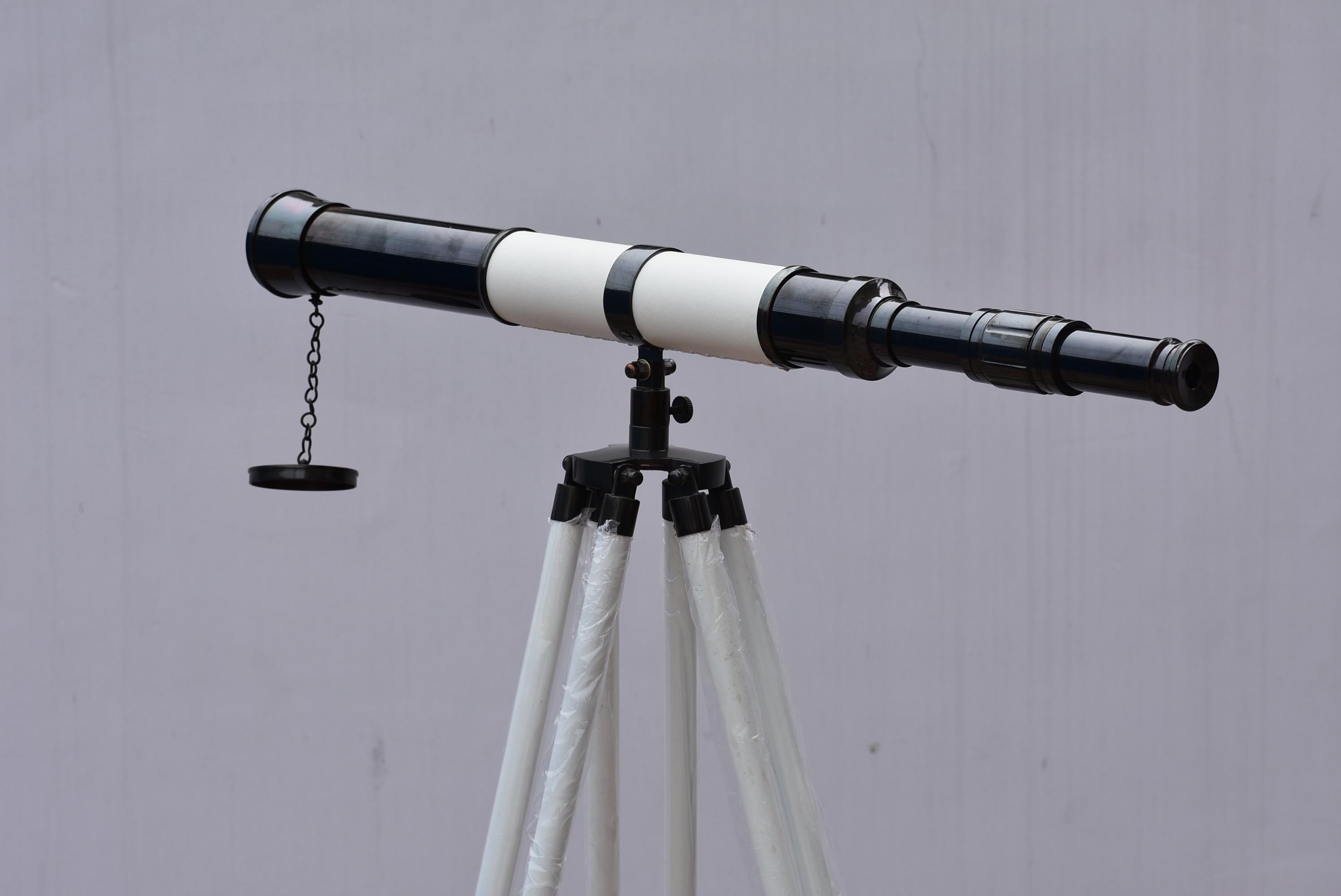 May include: A black and white telescope on a black tripod with white legs. The telescope has a chain and lens cap. The tripod is adjustable.