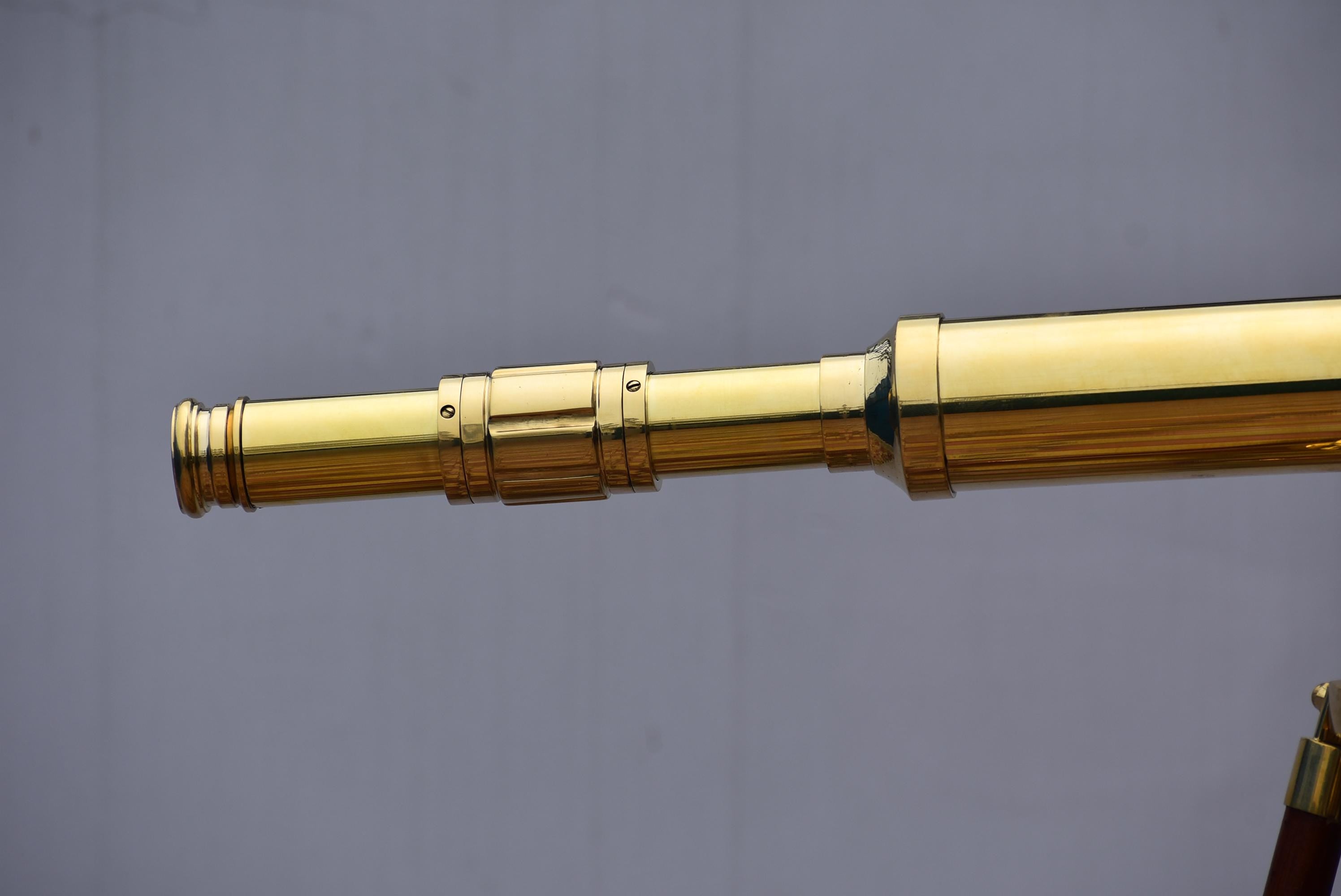 May include: A polished brass telescope with multiple extending sections. The telescope has a classic design with a warm, golden hue. The image shows the telescope's barrel and a portion of its wooden stand.