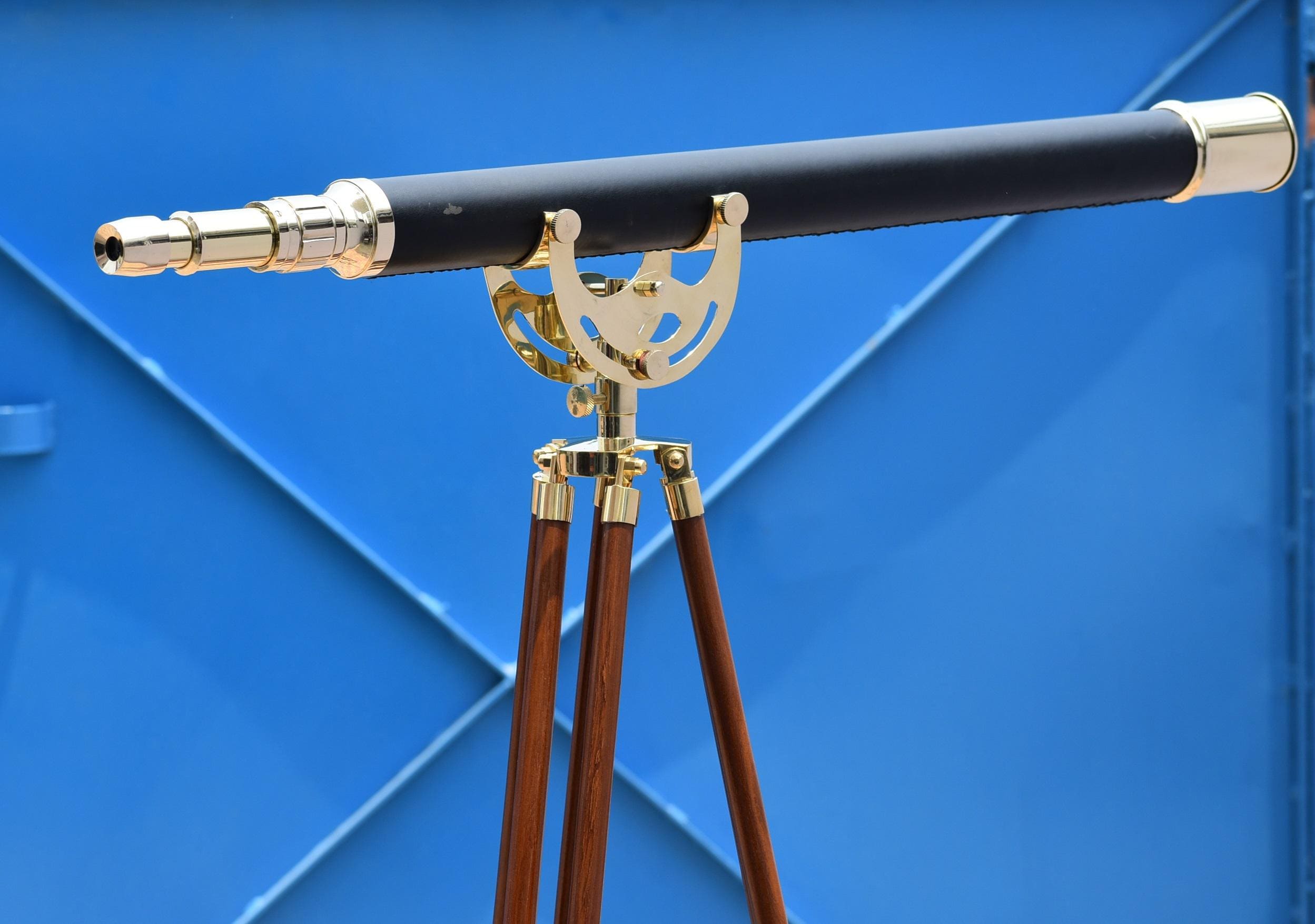 May include: A black telescope with gold-colored accents and a brass tripod. The telescope has a long, cylindrical barrel and is mounted on a wooden tripod with gold-colored metal fittings. The background is a solid blue.