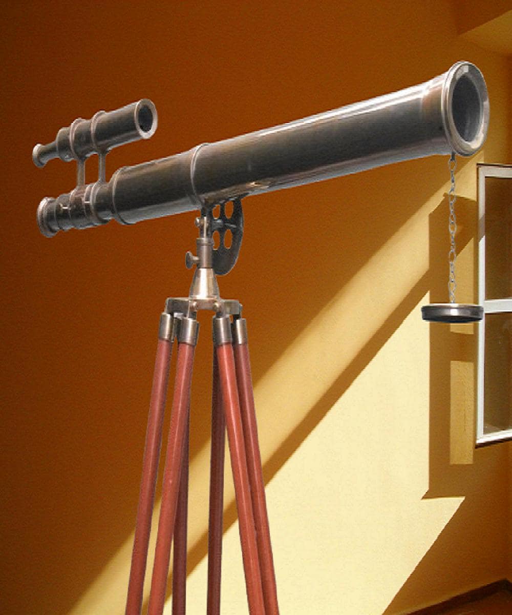 May include: A vintage telescope with a dark metallic finish, mounted on a wooden tripod. The telescope has a long barrel and an attached smaller scope. The tripod legs are reddish-brown. A small, circular weight hangs from the telescope.