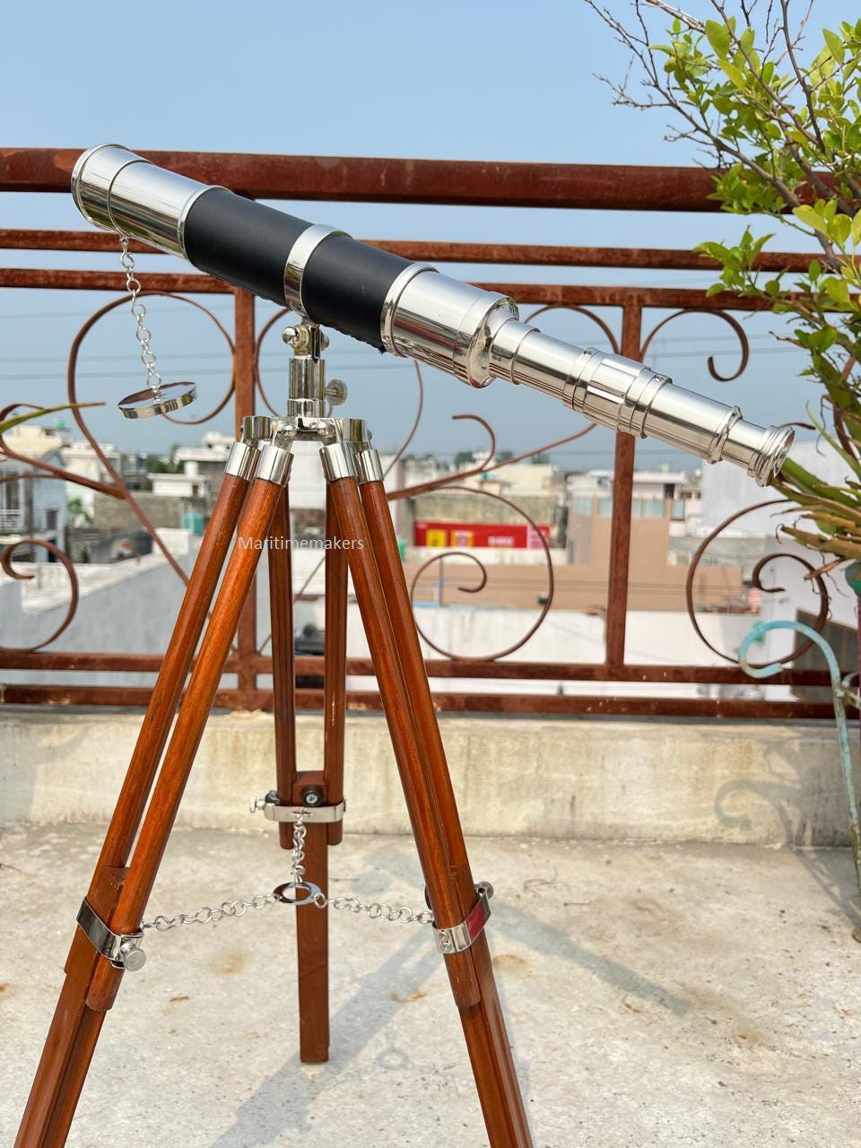 May include: A vintage-style telescope with a polished metal finish and a black leather grip. The telescope is mounted on a wooden tripod with metal accents. The tripod legs are a rich brown color. The image includes the text "Maritimemakers".
