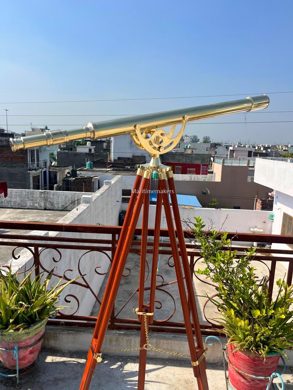 Può includere: Un telescopio in ottone montato su un treppiede in legno. Il telescopio ha una canna lunga e cilindrica ed è sostenuto da un supporto decorativo in ottone. Le gambe del treppiede sono di colore marrone rossiccio scuro. Il telescopio è allestito all'aperto.