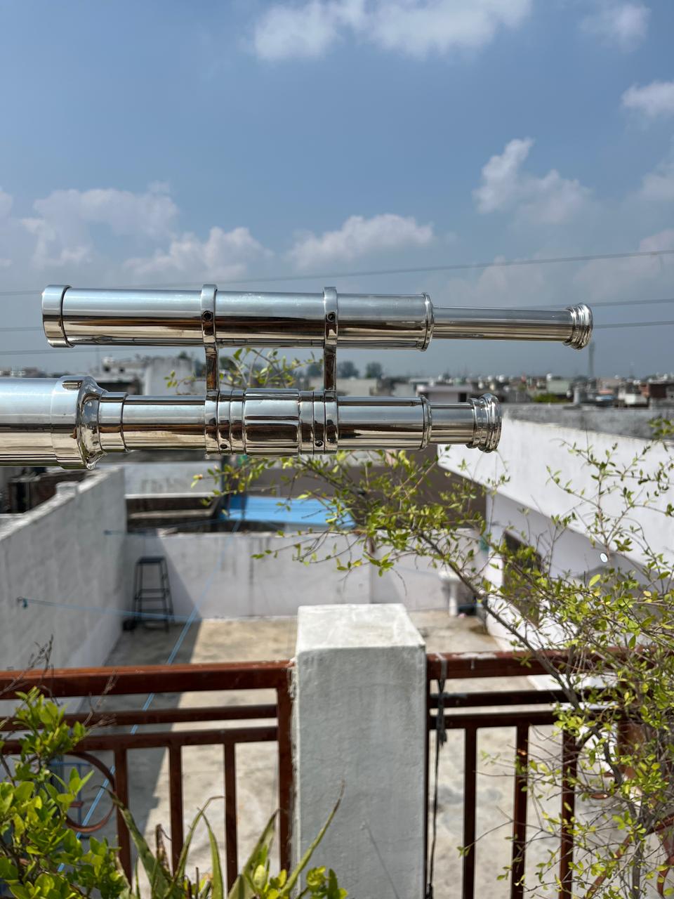 May include: Two polished silver telescopes are mounted horizontally, showcasing a classic design. The telescopes are set against a backdrop of a blue sky with scattered clouds, suggesting outdoor use. The design is reminiscent of nautical instruments.