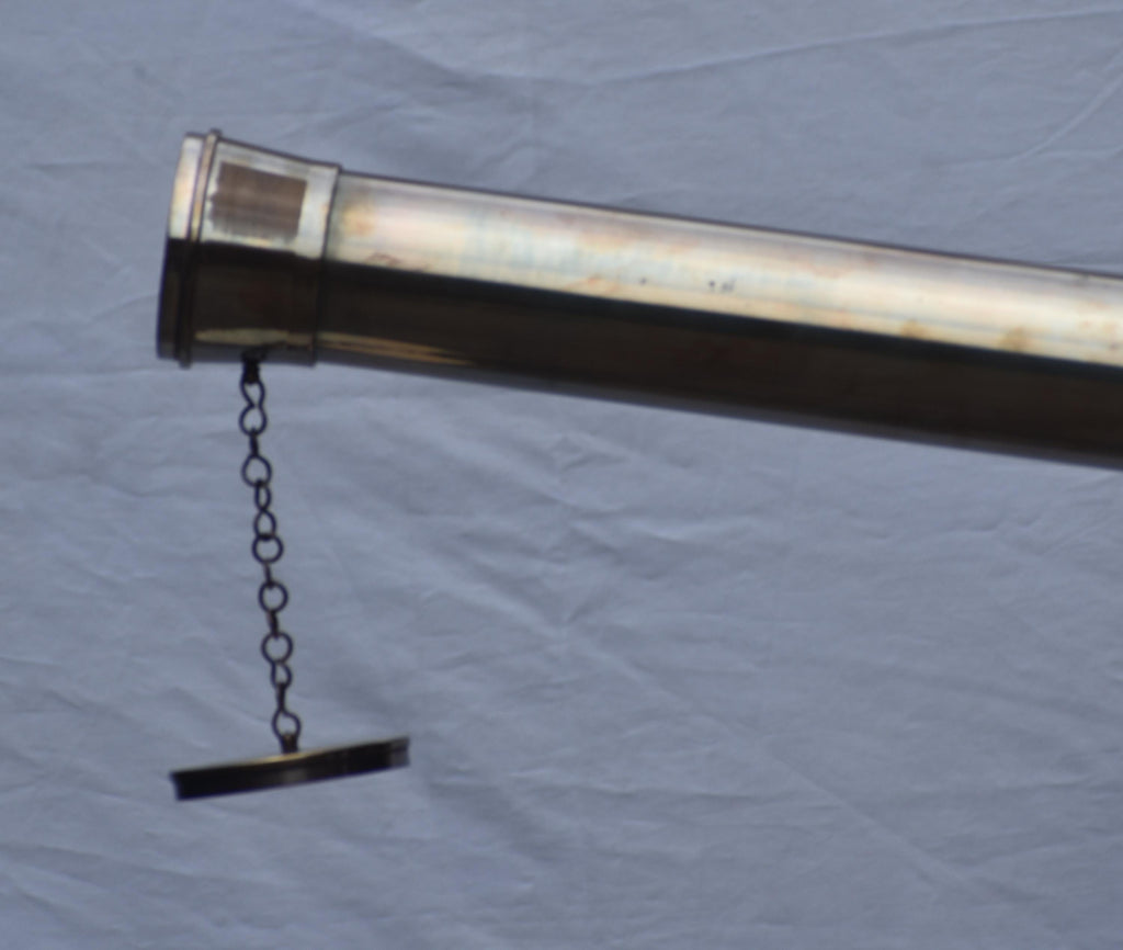 May include: A brass telescope with a chain and a rectangular cap. The telescope is angled diagonally, with the chain and cap hanging down. The brass has a polished, reflective surface.
