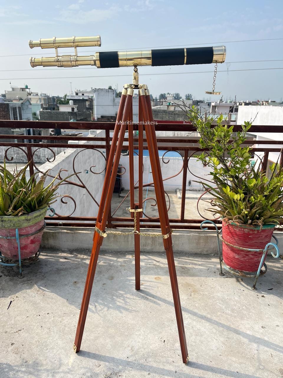 May include: A brass and black telescope on a wooden tripod. The telescope features a gold finish with black detailing, supported by a dark brown wooden tripod with brass fittings. The tripod is set up outdoors.