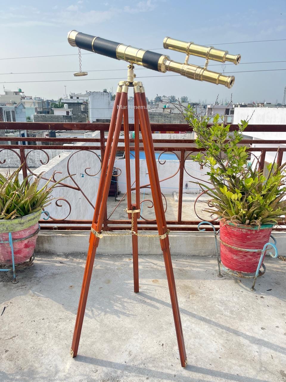 May include: A vintage brass and black telescope on a wooden tripod. The telescope has a long barrel with a secondary scope. The tripod is made of dark wood with brass accents and a chain, suitable for nautical or decorative use.