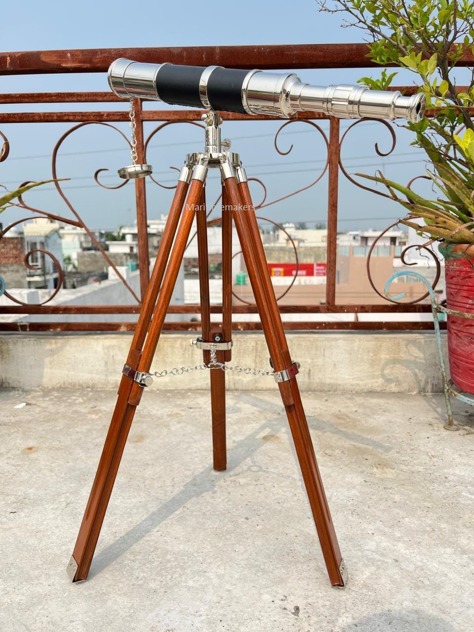 May include: A vintage-style telescope with a polished metal finish and black accents. The telescope is mounted on a wooden tripod with metal hardware. The tripod legs are a rich brown color, and the overall design evokes a classic nautical aesthetic.