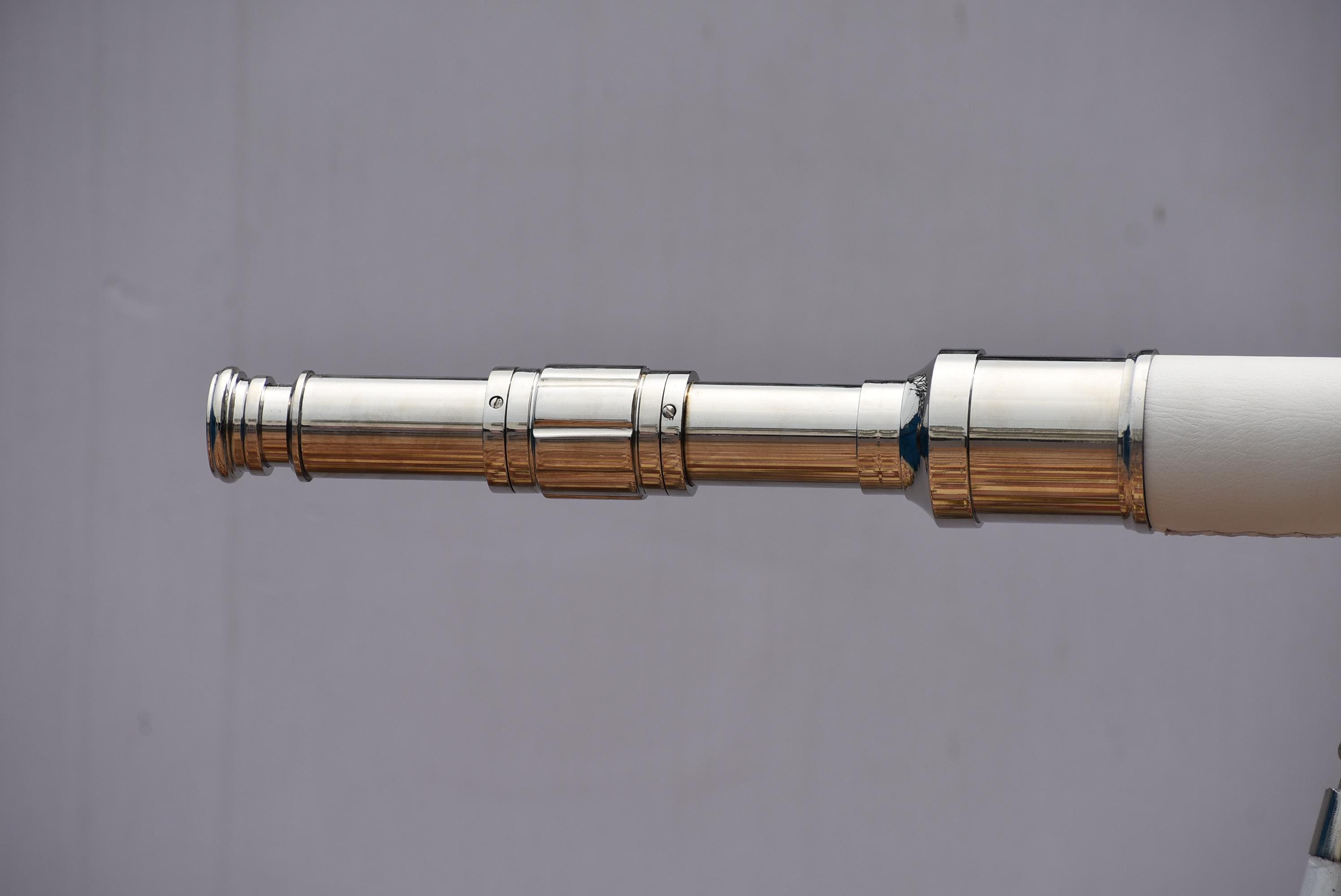 Può includere: Un telescopio argentato lucido con un'impugnatura bianca. Il telescopio è esteso e presenta più sezioni con un design dettagliato. Lo sfondo è di colore grigio.