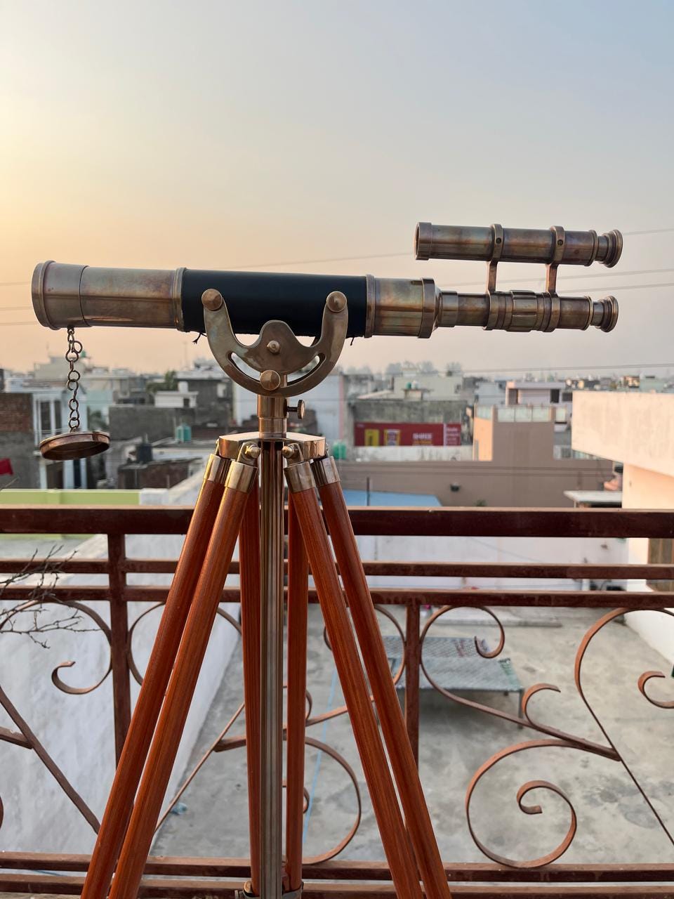 Può includere: Un telescopio in ottone in stile vintage con un barilotto rivestito in pelle nera, montato su un treppiede in legno. Il telescopio ha un mirino secondario e un tappo dell'obiettivo collegato a catena. Le gambe in legno sono rifinite con raccordi in ottone.