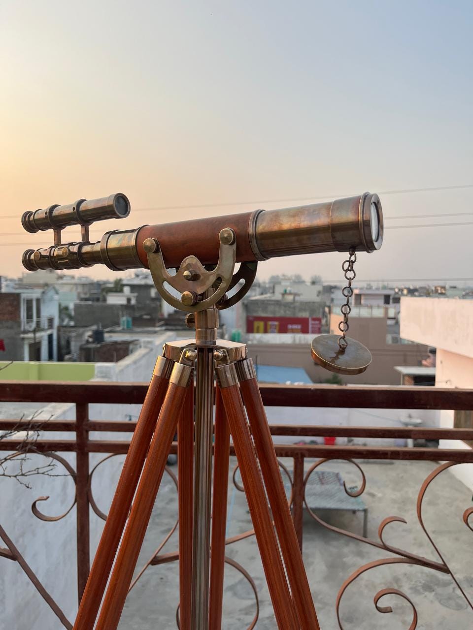 May include: A classic telescope on a wooden tripod. The telescope features a brass finish and a brown leather-wrapped barrel. The tripod legs are made of polished wood. The telescope is designed for observing distant objects.