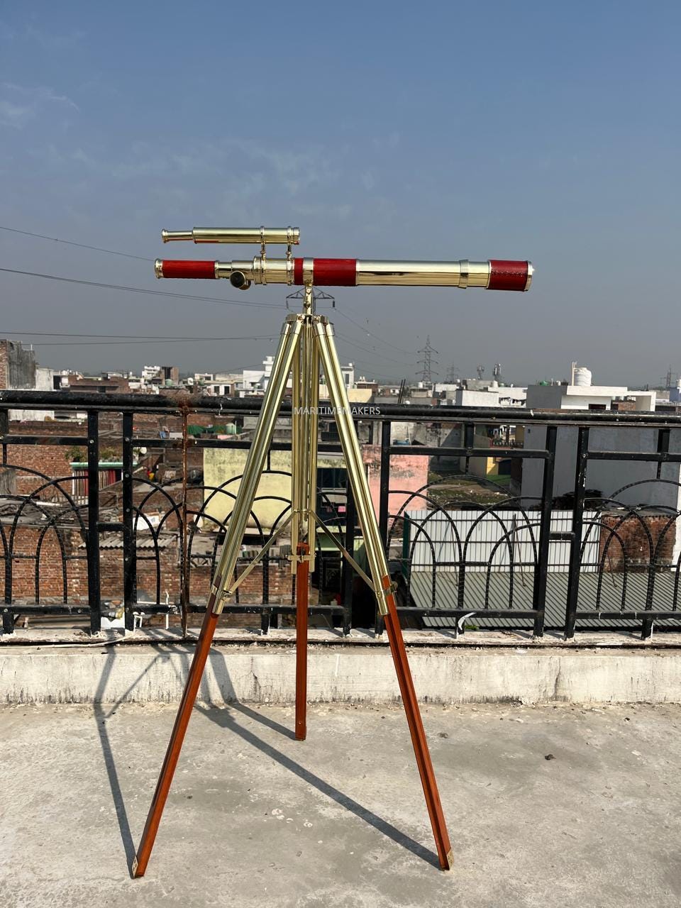 May include: A brass and red telescope on a wooden tripod. The telescope features a long, cylindrical barrel with red detailing and a smaller scope. The tripod has brass legs and wooden supports.