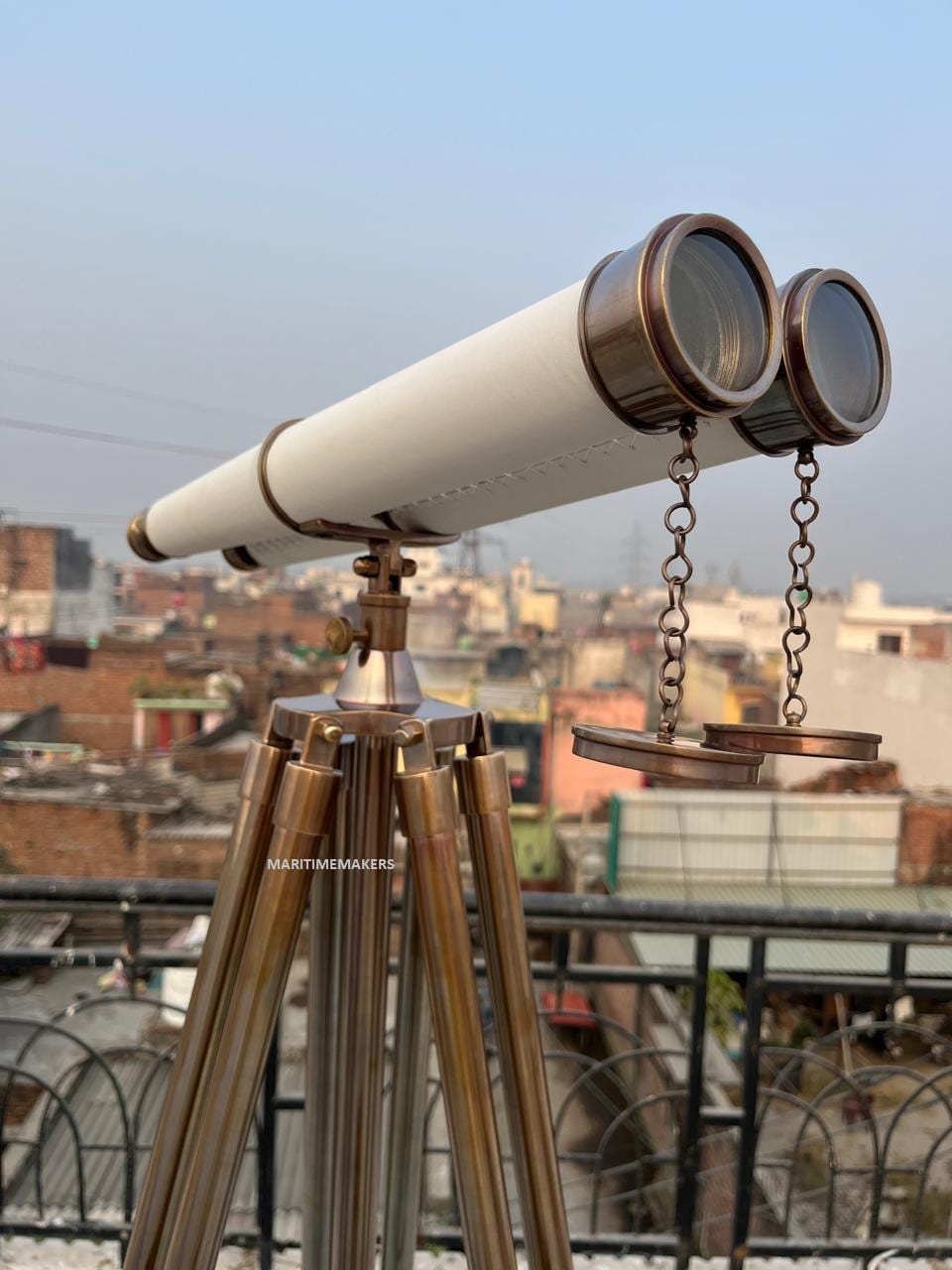 May include: A vintage brass and white telescope mounted on a tripod. The telescope features a white barrel and brass detailing. The tripod has three brass legs. The text "MARITIMEMAKERS" is visible on the tripod.