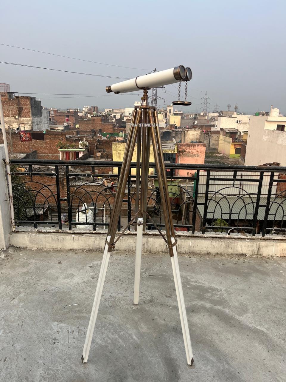May include: A vintage telescope with a cream-coloured barrel and brass accents. It is mounted on a tripod with white and brown legs. The telescope has a classic design, suitable for nautical or antique decor.